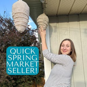 May include: Two beige, crocheted hanging lanterns with a spiral design are suspended outdoors. The lanterns are cone-shaped and appear handmade. The image includes the text "QUICK SPRING MARKET SELLER!" in a teal box.