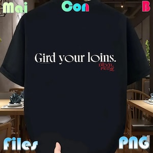Puede incluir: Camiseta negra con la frase blanca "Gird your loins." y el texto rojo "The Devil Wears Prada." La camiseta tiene mangas cortas y un corte holgado, ideal para un look casual.