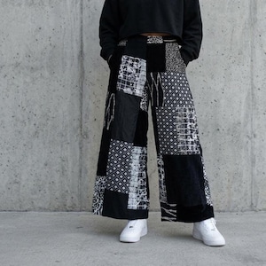 Può includere: Pantaloni ampi patchwork in bianco e nero. I pantaloni presentano vari motivi geometrici e testurizzati, creando un design unico. Abbinati a sneakers bianche e un top nero, sono un capo di tendenza.