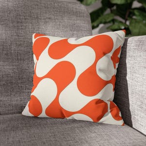 May include: A square throw pillow featuring a bold, repeating pattern of interconnected, fluid orange shapes against a solid off-white background. The design consists of smooth, curved lines that create a continuous, abstract wave-like motif across the surface.