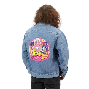 May include: Light blue denim jacket with a colorful graphic on the back featuring a cartoon band with the text "Jem and the Holograms". The graphic includes pink, yellow, purple, and blue colors. The jacket has a classic button-up design.