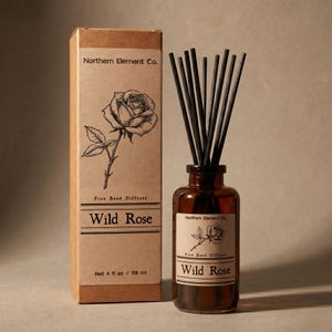 May include: A brown glass diffuser bottle with black reeds and a matching box. The box and bottle label read "Wild Rose" and feature a rose illustration. The bottle contains 118 ml of liquid.