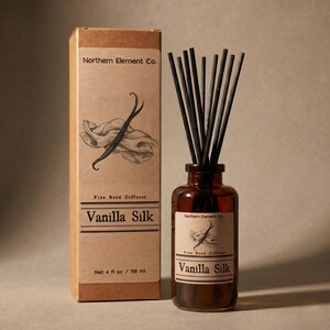 May include: A brown glass bottle with black reeds and a matching box. The box and bottle label read "Vanilla Silk" and "Northern Element Co." The box contains a drawing of a vanilla bean and fabric. The bottle contains 4 fl oz / 118 ml.