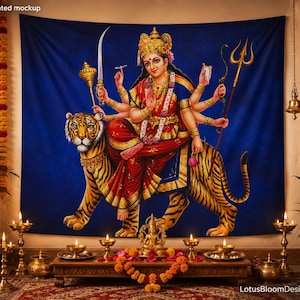 May include: A wall tapestry featuring a multi-armed deity dressed in a red and gold sari, seated atop a tiger against a deep blue background. The deity holds various symbolic items including a sword, mace, and trident, with a crown and jewelry.