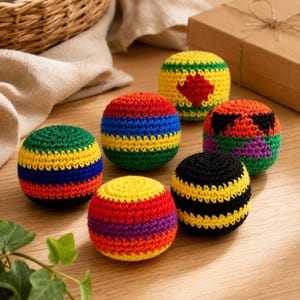 Puede incluir: Una colección de siete coloridas pelotas de malabares tejidas a ganchillo. Cada pelota presenta una combinación única de colores brillantes, incluyendo rojo, amarillo, verde, azul y negro. Las pelotas están dispuestas sobre una superficie de madera, sugiriendo un tema lúdico y artesanal.
