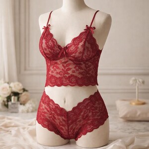 May include: A red lace lingerie set on a mannequin. The set comprises a bralette with thin straps and matching shorts. The bralette and shorts feature floral lace patterns and small bows, creating a delicate and romantic aesthetic.