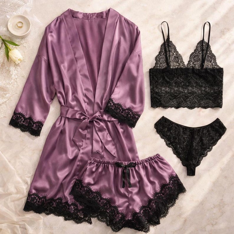 May include: A mauve satin lingerie set featuring a robe with black lace trim, a bralette, and shorts, both with black lace trim, and a matching thong. The bralette and thong are black.