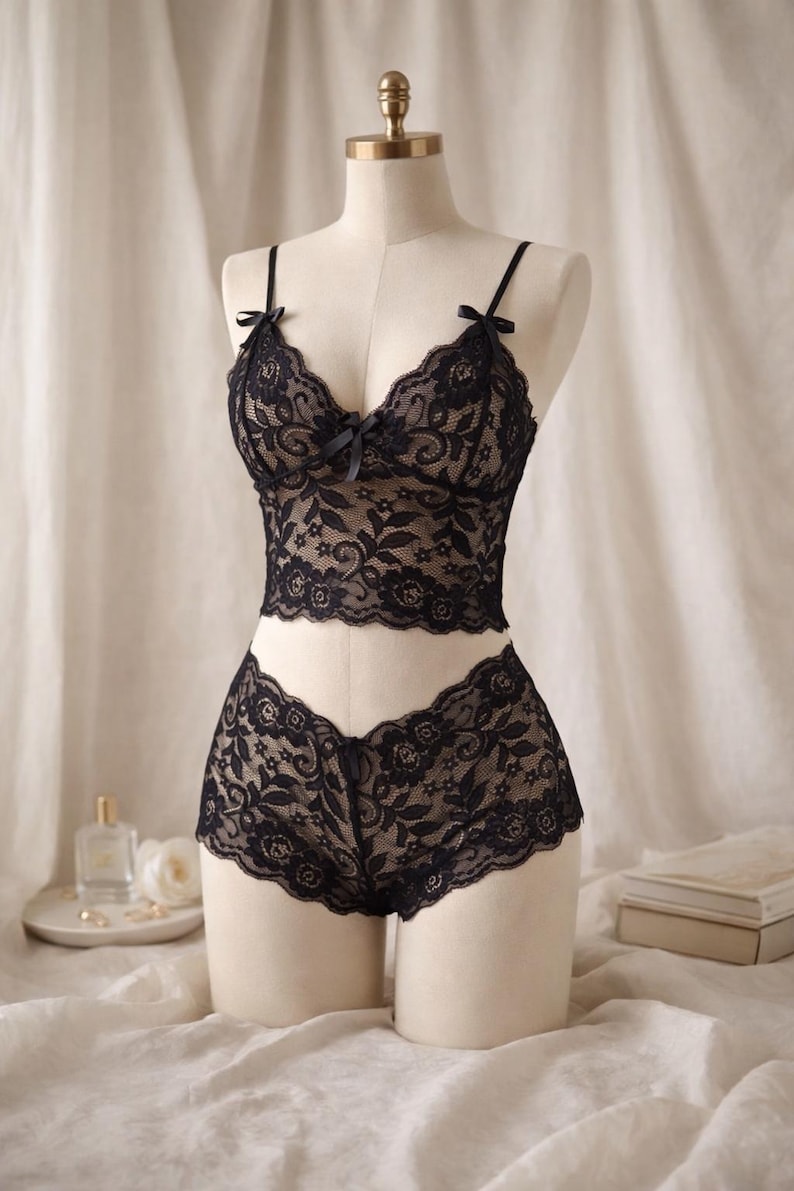 May include: Black lace lingerie set on a mannequin. The set features a camisole top with thin straps and a bow, and matching shorts. The delicate floral pattern is visible throughout the set.
