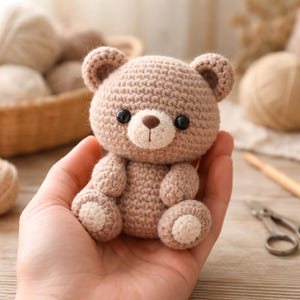 Op de afbeelding: Een handgemaakte gehaakte teddybeer in tinten bruin en crème. De beer heeft zwarte veiligheidsoogjes, een bruine neus en crèmekleurige accenten op de poten. Het is een klein speelgoed- of decoratieartikel.