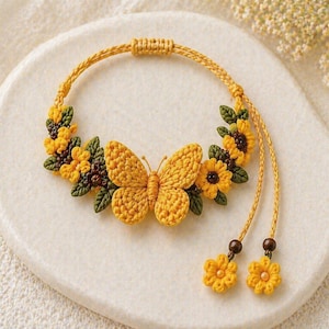 May include: A handcrafted yellow crochet bracelet featuring a butterfly and floral design. The bracelet is adorned with yellow flowers, green leaves, and a butterfly in the center. The bracelet is displayed on a white surface.