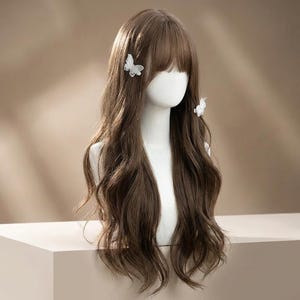 May include: A brown wig with long, wavy hair and a blunt fringe, styled on a mannequin head. Two white butterfly hair clips are placed on the wig. The wig is displayed on a white surface against a neutral background.
