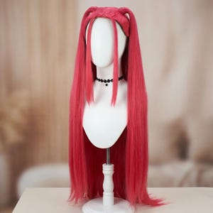 Könnte beinhalten: Eine leuchtend pinke Perücke mit langem, glattem Haar, das mit zwei kleinen Brötchen oben und Ponyfransen gestylt ist. Die Perücke wird auf einem weißen Schaufensterpuppenkopf mit einer schwarzen Halskette präsentiert. Für Cosplay oder Kostüm.
