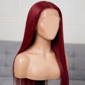 May include: A mannequin head showcasing a long, straight wig. The wig is a deep burgundy colour, with a natural-looking hairline. The hair is styled to fall straight down, highlighting its length and shine. The mannequin is set against a neutral background.