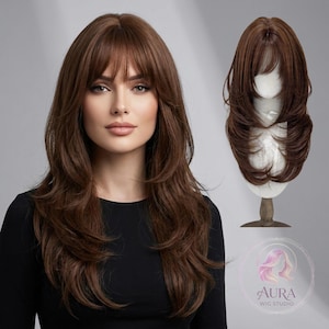 Puede incluir: Una mujer con cabello largo, castaño y en capas con flequillo. Una segunda peluca se muestra en una cabeza de maniquí. El logotipo de Aura Wig Studio está en la esquina inferior derecha. El cabello está peinado con ondas suaves.