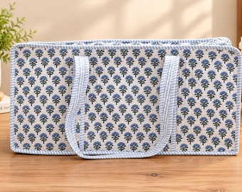May include: A rectangular quilted storage bag featuring a repeating pattern of small blue flowers on a white background. The bag is finished with light blue and white striped fabric trim along the edges and includes two matching striped carry handles.
