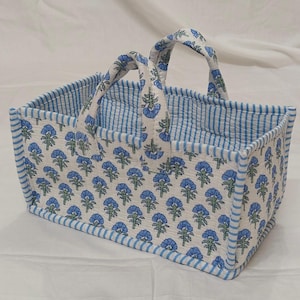 May include: A rectangular fabric storage basket featuring a white base with a repeating blue floral pattern. The basket has two matching fabric handles and is trimmed with blue and white striped fabric along the edges and interior lining.