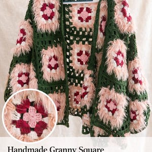 Könnte beinhalten: Handgemachte, übergroße Granny-Square-Häkeljacke. Die Jacke hat ein grünes, rosa und bordeauxfarbenes Farbschema. Das Design umfasst quadratische Muster mit flauschigen rosa Akzenten. Der Text auf dem Bild lautet "Handmade Granny Square Crochet Jacket ONE SIZE - Oversized."
