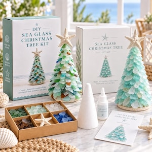 Op de afbeelding: Een DIY-pakket voor een kerstboom van zeeglas met twee witte dozen met tekst, twee gemonteerde boompjes met zeesterren, een kartonnen doos met vakjes voor gekleurd zeeglas, een witte kegel, lijm en een instructiekaart.