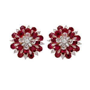 May include: A pair of circular cluster earrings featuring a central arrangement of clear pear-shaped and baguette-cut stones surrounded by multiple layers of deep red oval-cut stones, all set in a metallic frame with a prong-style mounting design.