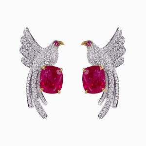 May include: A pair of bird-shaped earrings crafted from silver-toned metal, featuring pavé-set white stones covering the wings and tail. Each bird has a small red stone for an eye and holds a large, square-cut vibrant red gemstone in its talons.