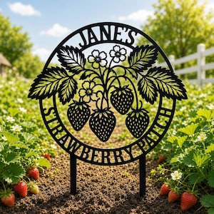 May include: Black metal garden stake with the text "JANE'S STRAWBERRY PATCH" in a circular design. The design features strawberries, leaves, and flowers. The stake is in a garden with strawberry plants.