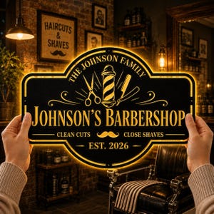 Könnte beinhalten: Ein schwarzes rechteckiges Schild mit abgerundeten Kanten und goldener Schrift, die THE JOHNSON FAMILY JOHNSON'S BARBERSHOP CLEAN CUTS CLOSE SHAVES EST. 2026 lautet, mit einer Grafik von Barber-Pole, Schere und Rasiermesser.