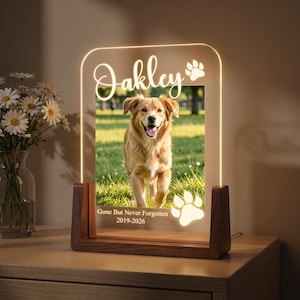 Op de afbeelding: Een rechthoekig, verlicht gedenkbord van acryl met een houten voet, voorzien van een foto van een gouden hond. De tekst luidt Oakley, Gone But Never Forgotten, 2019-2026, vergezeld van twee pootafdruk-iconen op het heldere oppervlak.