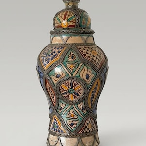 Peut inclure: Un pot en céramique avec couvercle, orné de motifs géométriques et floraux peints à la main dans des tons turquoise, jaune, bleu et marron. Le récipient est entouré d'une structure en filigrane métallique argenté soulignant les panneaux.