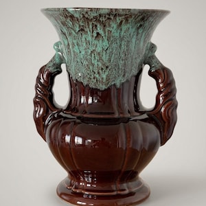 Può includere: Un vaso in ceramica caratterizzato da una base marrone scuro lucida con nervature verticali e due manici laterali decorati. La parte superiore del vaso e i manici presentano un caratteristico effetto di smalto a goccia turchese e marrone.