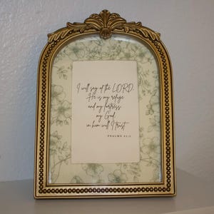 May include: An arched gold picture frame with a beaded border and a decorative top crest. Inside, a white card features the black text: I will say of the LORD. He is my refuge and my fortress, my God; in him will I trust. PSALMS 91:2.
