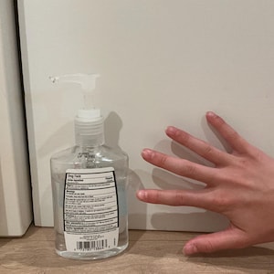 May include: A clear plastic bottle of hand sanitizer featuring a white pump dispenser and a rectangular label on the front. The label contains black text detailing drug facts, active ingredients, and warnings, along with a barcode at the bottom.