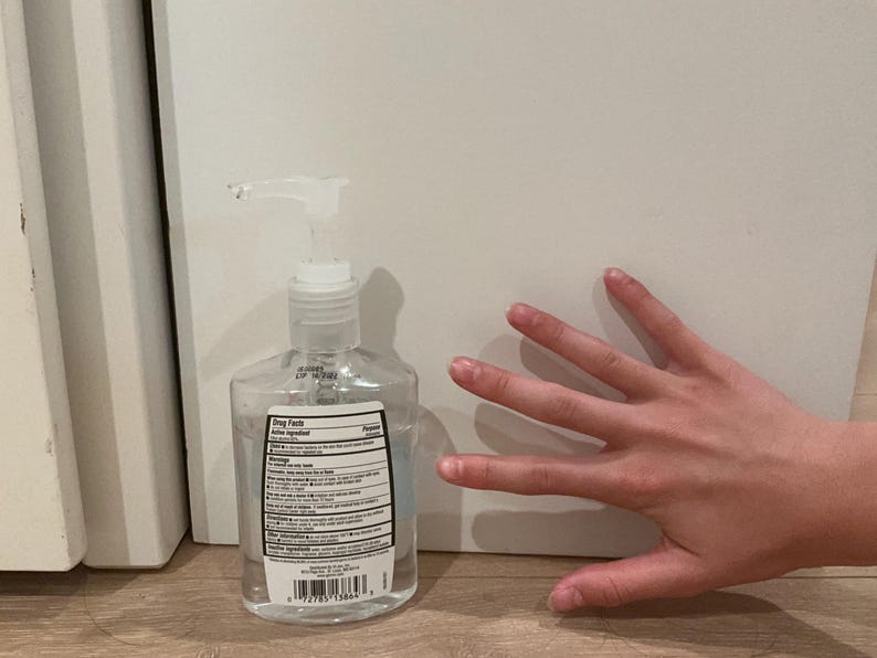 May include: A clear plastic bottle of hand sanitizer featuring a white pump dispenser and a rectangular label on the front. The label contains black text detailing drug facts, active ingredients, and warnings, along with a barcode at the bottom.
