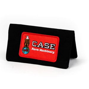 Puede incluir: Cartera negra con un parche rojo que muestra un águila blanca de pie sobre un globo terráqueo con el texto "CASE Farm Machinery".
