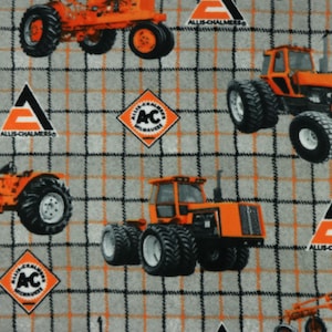 May include: A grey and orange fabric with a repeating pattern of orange tractors and the Allis-Chalmers logo. The tractors are in various sizes and positions, and the logo is in a diamond shape.