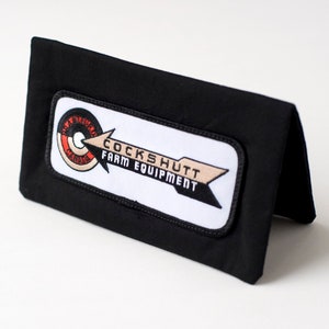 May include: Black fabric wallet with a white patch featuring a red and white logo with the text "Cockshutt Farm Equipment".