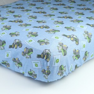 May include: A blue fitted sheet with a repeating pattern of green and black tractors. The tractors have the John Deere logo on them.