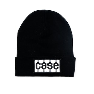 May include: Black beanie hat with a white rectangular patch. The patch features the word "CASE" in a stylized font. The hat is made of a knitted material and is suitable for cold weather.