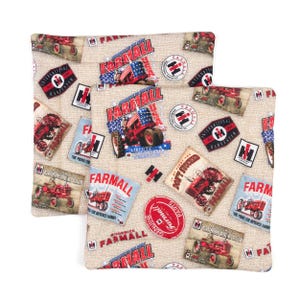 Puede incluir: Dos fundas de cojín de tela beige con un estampado de tractor Farmall rojo, blanco y azul. El estampado presenta el logotipo de Farmall, las palabras "Farmall" y "Liberty", y un tractor con una bandera estadounidense roja, blanca y azul en el lateral.