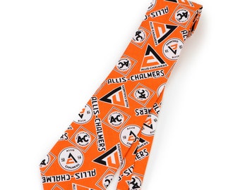 Puede incluir: Corbata naranja con un patrón repetido del logotipo de Allis-Chalmers en blanco y negro. La corbata presenta el texto "ALLIS-CHALMERS" y el logotipo "AC". Un accesorio clásico.