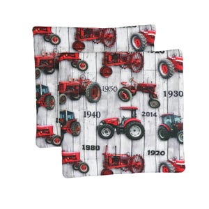 Puede incluir: Dos cuadrados de tela con un patrón repetido de tractores rojos sobre un fondo blanco y gris con vetas de madera. Los años 1920, 1930, 1940, 1950, 1980 y 2014 están impresos en la tela.