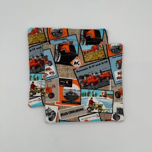Puede incluir: Dos agarraderas de olla de tela naranja y negra con un fondo de arpillera. Las agarraderas de olla presentan un collage de anuncios vintage de tractores Allis-Chalmers. El texto en las agarraderas de olla incluye "Dynamic D-17 and D-14", "Allis-Chalmers" y "New Choice for the Farm".