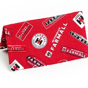 May include: Red fabric wallet with a repeating pattern of the McCormick Farmall logo and text. The logo features a red tractor with a white 'H' and the text 'McCormick Farmall International Harvester'.