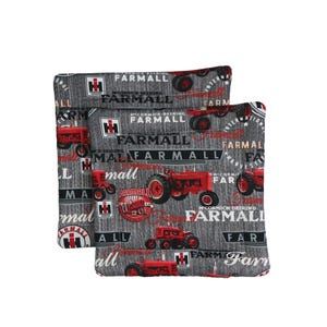 Puede incluir: Dos artículos de tela con temática Farmall con un fondo gris e ilustraciones de tractores rojos. La tela tiene un estampado con la palabra "FARMALL" y el logotipo de Farmall. Los artículos son probablemente almohadas o cojines.