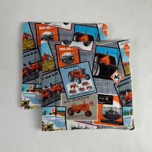 Puede incluir: Dos agarraderas de olla de tela azul y blanca con un estampado de tractor vintage. El estampado presenta tractores naranja y rojo con el texto "WD-45", "Allis-Chalmers", "new champion", "Dynamic" y "Model G".