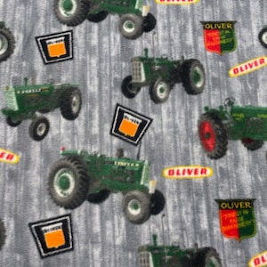 May include: A gray fabric with a repeating pattern of green and black tractors. The tractors have the word "Oliver" on them. The fabric also has a repeating pattern of red, white, and green logos with the words "Oliver" and "The Finest in Farm Machinery".