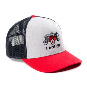 Könnte beinhalten: Eine graue und rote Trucker-Kappe mit schwarzem Netzrücken. Die Kappe zeigt ein gesticktes Bild eines roten Ford 8N Traktors mit dem Text "Ford 8N".