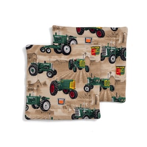 May include: Two tan fabric pillow covers with a green tractor pattern. The tractors are green and black with the word "Oliver" on them. The background is tan with a brown and white pattern.