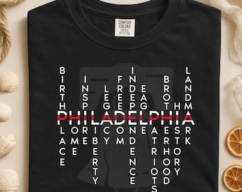 May include: Black t-shirt with a graphic design featuring the word "PHILADELPHIA" in red, surrounded by a word puzzle. The shirt includes the text "USA 250 - 1776-2026". Made by Comfort Colors.