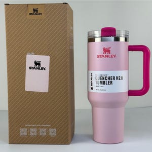 May include: A pink Stanley Quencher H2.0 Tumbler with a matching handle and lid. The tumbler is 40 oz and comes with a cardboard box. The box has the Stanley logo and product information.