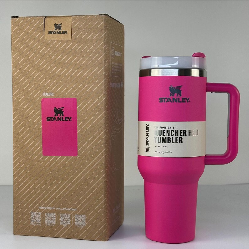 May include: A pink Stanley Quencher H2.0 Tumbler with a handle and a white and silver lid. The tumbler is 40 oz. and comes with a matching pink box. The Stanley logo is visible on the tumbler and the box.